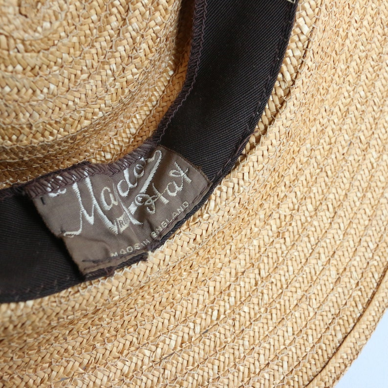 Op de afbeelding: Een close-up van een strohoed met een bruin band en een label met de tekst "Made in England"