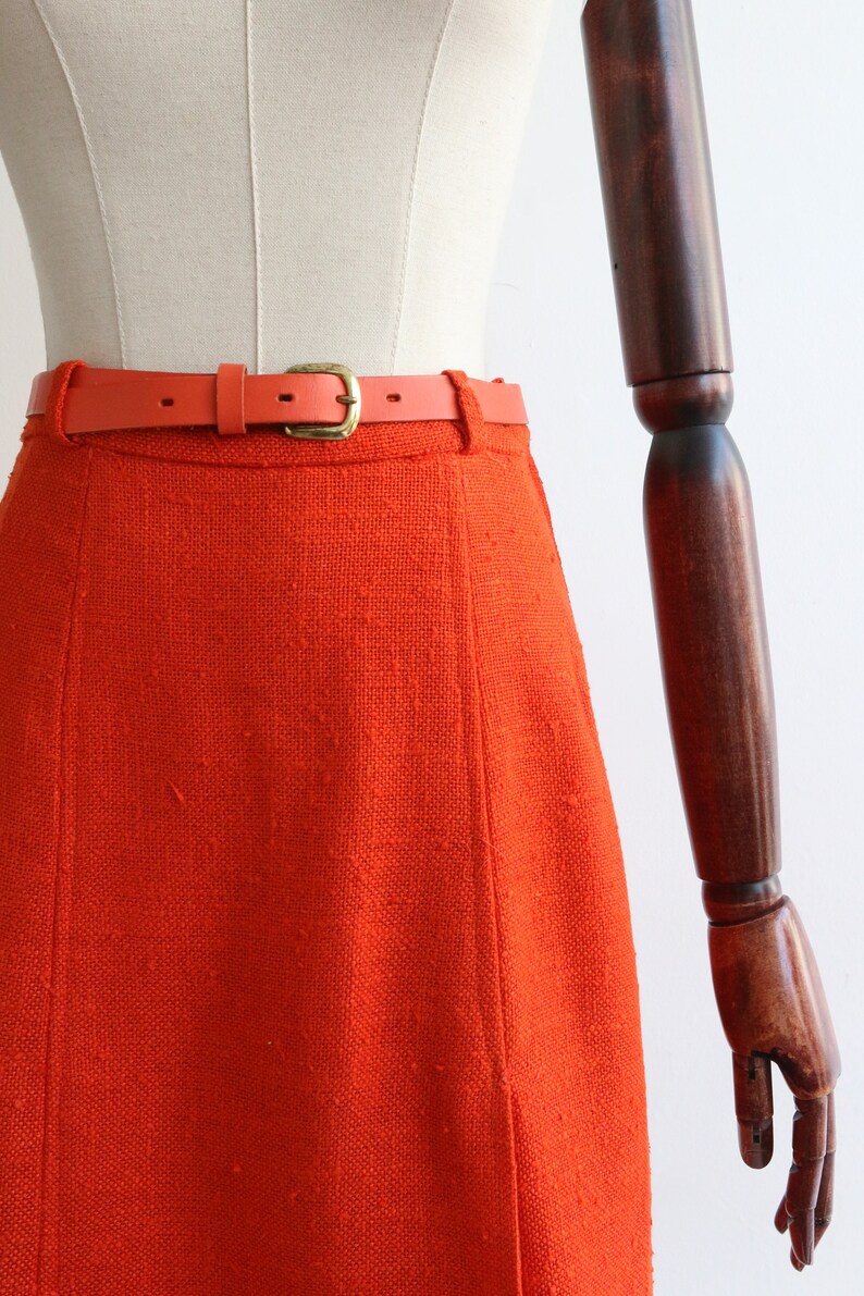 May include: A bright orange skirt with a thin, orange leather belt and a gold buckle.