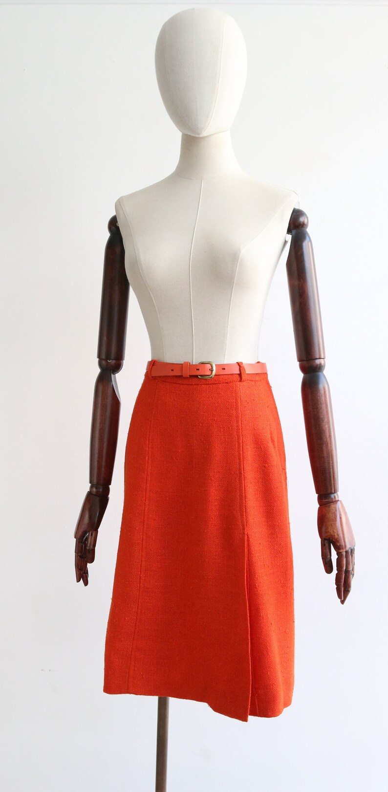 May include: A bright orange skirt with a brown leather belt. The skirt is knee-length and has a straight silhouette.