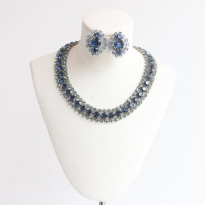 May include: A blue and light blue rhinestone necklace and earrings set. The necklace is a double row of graduated rhinestones. The earrings are a cluster of rhinestones.