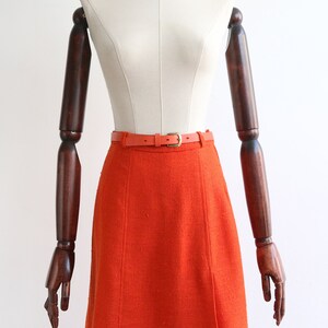 May include: A bright orange A-line skirt with a matching orange belt. The skirt is made of a textured fabric and has a simple, classic design.
