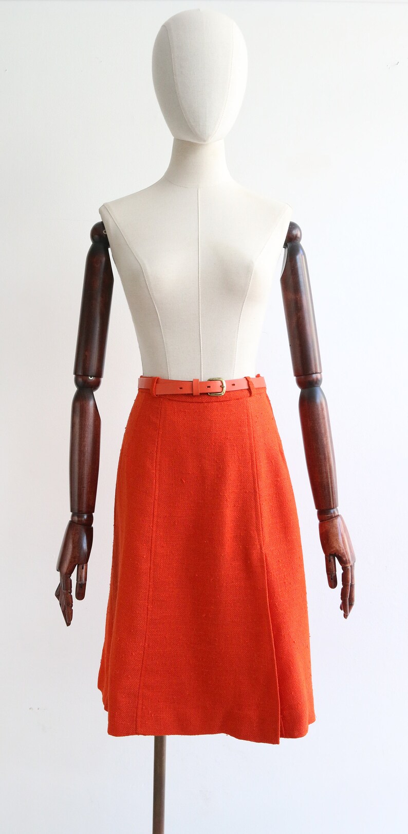 May include: A bright orange A-line skirt with a matching orange belt. The skirt is made of a textured fabric and has a simple, classic design.