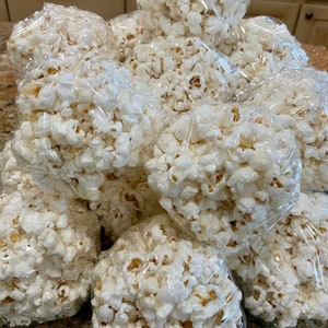 May include: A pile of popcorn balls wrapped in clear plastic wrap. The popcorn balls are white and have a slightly yellow hue.