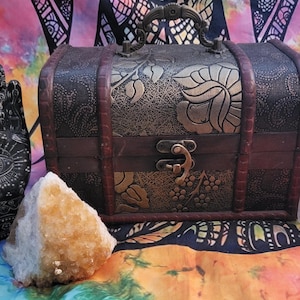May include: A wooden treasure chest with an ornate floral design, a black hand sculpture with an eye design, a large clear crystal, and a white crystal tower.