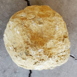 May include: A large, round, yellow-brown geode with a rough, textured surface.