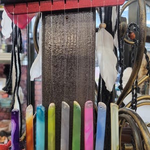 May include: A wooden wind chime with eight agate slices hanging from it. The agate slices are in various colors, including purple, orange, blue, green, gray, pink, light blue, and white.