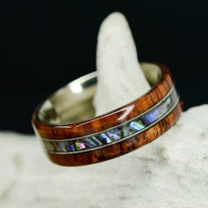 May include: A wooden ring with a silver band and a strip of iridescent abalone shell inlay.