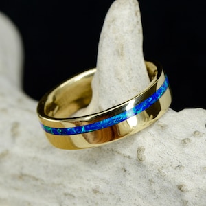 May include: A gold band with a thin blue opal inlay. The ring is on a white background.