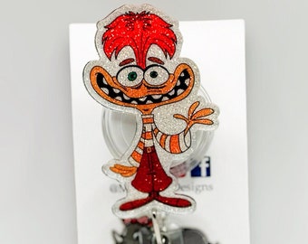 May include: A sparkly red and orange cartoon character with a big smile and a white background. The character is attached to a clear plastic retractable badge holder with a sparkly silver and white round charm.