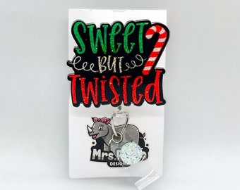 Op de afbeelding: Een witte achtergrond met een kerstthema badgehouder met een neushoorn met een roze strik en de tekst "Sweet but Twisted". De badgehouder heeft een glinsterende zilveren hanger.