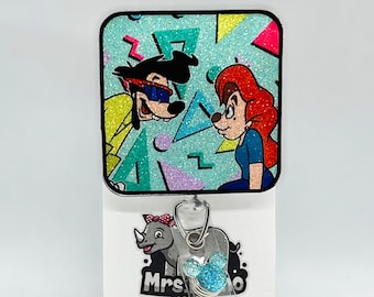 May include: A blue and green glitter badge reel with a cartoon image of a dog and a woman. The reel has a clear plastic strap and a blue glitter Mickey Mouse head charm. The text "Mrs. Designs" is printed on the bottom of the reel.