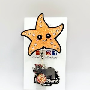 May include: A sparkly orange starfish with a smiling face is attached to a clear badge holder with a glitter-covered rhino logo. The badge holder is attached to a silver chain. The text "@MrsRhinoDesigns" is printed on the white background.