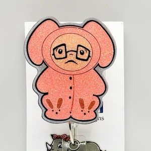 May include: Pink glitter badge reel with a cartoon character wearing a pink onesie and glasses. The reel is attached to a clear plastic retractable badge holder. The text "Mr. Rhino" is visible on the badge holder.