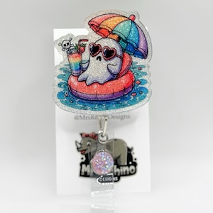 May include: A glittery badge reel featuring a cartoon ghost wearing heart-shaped sunglasses, floating on a red and purple inner tube under a rainbow umbrella. The ghost is holding a colorful drink with a skull and crossbones. A rhino design is at the bottom.