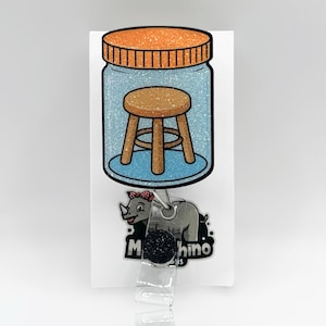 May include: A badge reel featuring a cartoon image of a small wooden stool inside a jar with a glittery orange lid. Below the jar is a gray rhino with a red bow. The reel has a black glittery top.