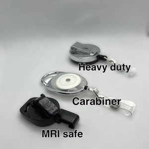May include: Three different types of retractable badge reels. The top reel is silver and has the text "Heavy duty". The middle reel is silver and has the text "Carabiner". The bottom reel is black and has the text "MRI safe".