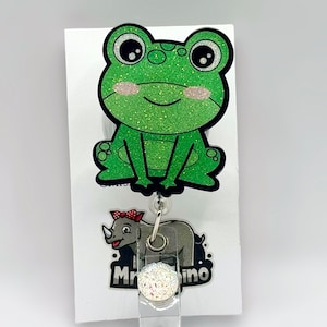 May include: A green glitter frog cartoon character badge reel with a white glitter circle and a rhino cartoon character with the text "Mr. Rhino" on the back.