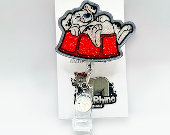 May include: A red glitter dog bed with a white dalmatian dog laying in it. The dog bed is attached to a clear plastic retractable badge holder with a silver clip. The badge holder has a white glitter circle with the text "Little Rhino Designs" on it.