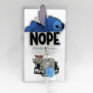 May include: A blue glitter badge reel featuring the character Stitch from Lilo & Stitch, lying down with the word "NOPE" in bold, black letters. A rhino graphic is below the reel.