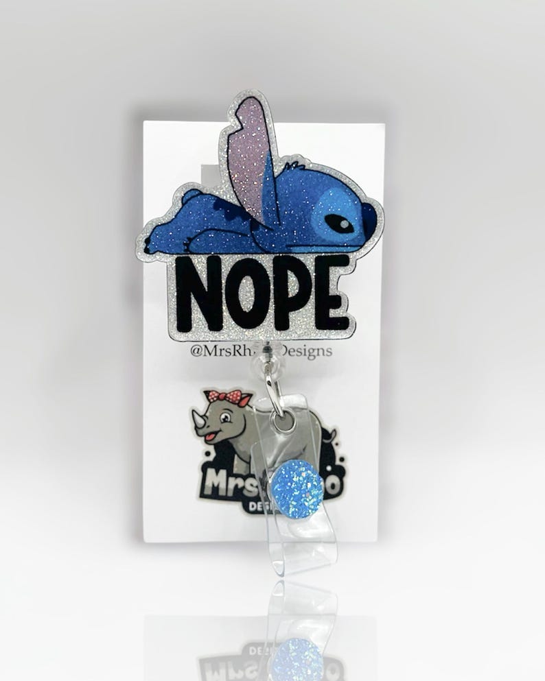 May include: A blue glitter badge reel featuring the character Stitch from Lilo & Stitch, lying down with the word "NOPE" in bold, black letters. A rhino graphic is below the reel.