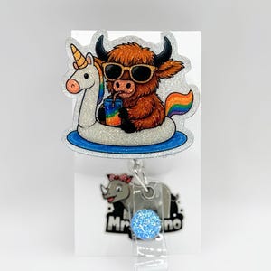 May include: A badge reel featuring a cartoon Highland cow wearing sunglasses and drinking from a rainbow-colored cup while floating on a unicorn float. The reel has a rhino design and a blue glitter accent.