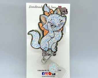 May include: A sparkly white glitter cat with a pink bow on its head, holding a paw to its face. The cat is on a white card with the text "Handmade with love" and a small rhino logo. The card also includes social media handles for the creator, "@mrsrhinodesigns".