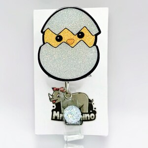 May include: A silver glitter chick hatching from an egg with a clear retractable badge holder with a sparkly crystal charm. The charm has the text "Mr. Rhino" on it.