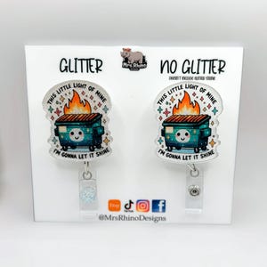 Pu&ograve; includere: Due porta badge con un design a cassonetto. Uno &egrave; etichettato "Glitter" e l'altro "No Glitter". Ogni porta badge ha il testo "This little light of mine, I'm gonna let it shine". I porta badge sono su un espositore bianco.