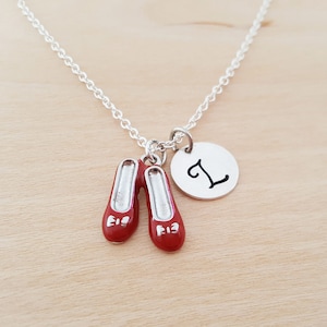 May include: Silver necklace with a red ruby slipper charm and a silver charm with the letter L.