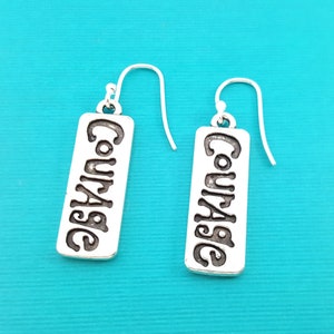 May include: Silver dangle earrings with the word "Courage" engraved on each rectangular charm.