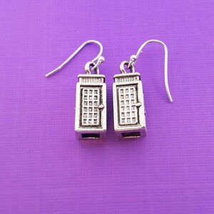 May include: A pair of silver earrings with a detailed design of a door. The earrings are hanging from silver hooks.