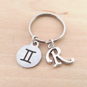 May include: Silver keychain with a Gemini zodiac symbol charm and a letter R charm.
