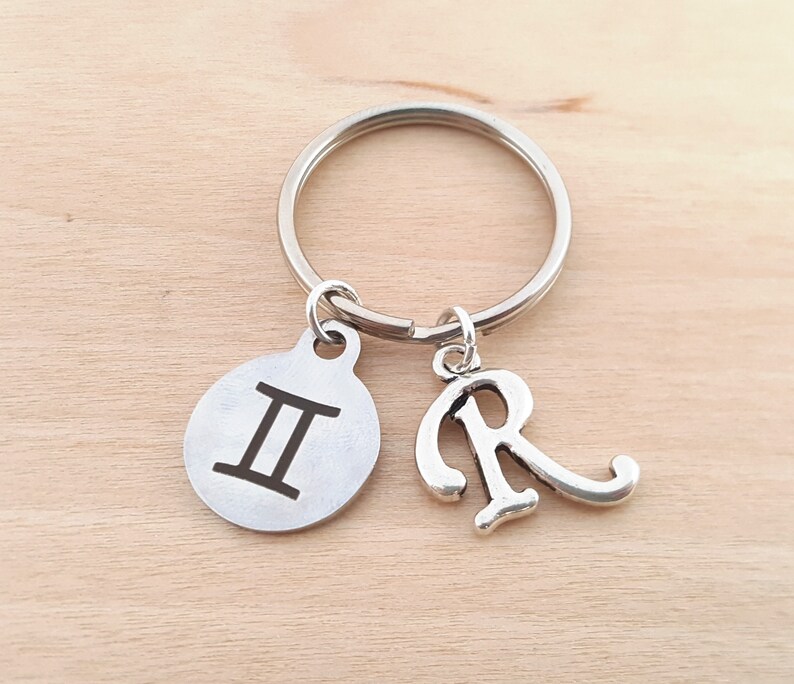 May include: Silver keychain with a Gemini zodiac symbol charm and a letter R charm.