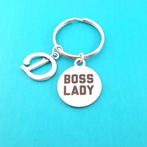 May include: Silver keychain with a charm that says "Boss Lady" and a letter D charm. The keychain is on a turquoise background.