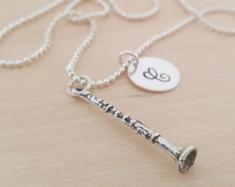 May include: A silver necklace with a silver clarinet charm and a silver disc charm with the letter "G" engraved on it.