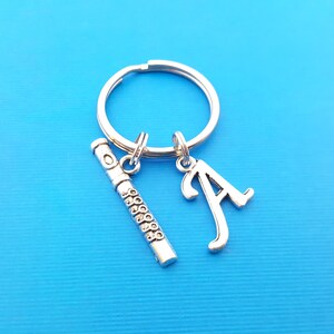 May include: Silver keychain with a silver flute charm and a silver letter A charm. The keychain is on a blue background.