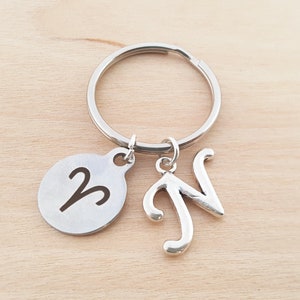 May include: Silver keychain with a round charm featuring the astrological symbol for Aries and a charm with the letter N.