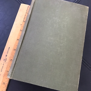 May include: A green hardcover book with a textured cover. The book is closed and lying flat on a black surface.