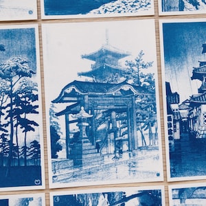 以下が含まれることがあります： 日本の建築や風景を青いインクで描いた長方形のアートプリントのコレクション。中央のプリントには、松の木に囲まれた多層の塔、伝統的な門、石灯籠が描かれています。