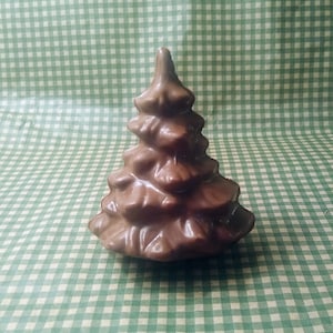 Puede incluir: Una pequeña figura decorativa de árbol de Navidad marrón. El árbol tiene una superficie texturizada y una parte superior puntiaguda. Se encuentra sobre un fondo a cuadros verdes y blancos.