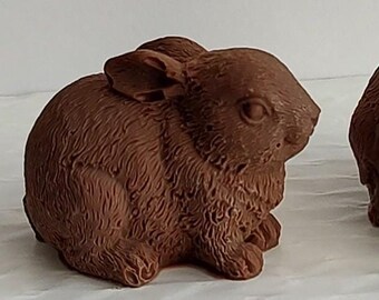 May include: Two brown chocolate bunny figurines. The bunnies are sitting with their heads down and their ears are perked up.