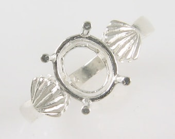Könnte beinhalten: Silberne Ringfassung mit einem großen ovalen Mittelstück und zwei kleineren muschelförmigen Akzenten auf jeder Seite.