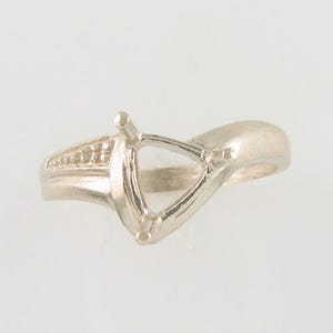 May include: A silver-toned ring with a triangular setting and a band that curves around the finger. The ring has a small row of accent stones on one side of the setting. The ring is designed to hold a gemstone.