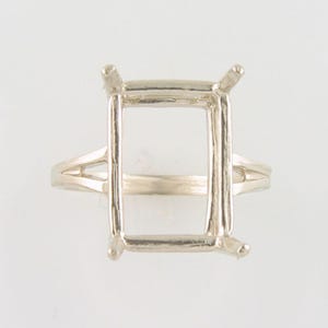 May include: A silver ring setting with a square shaped bezel for a gemstone. The ring has a delicate band with a split shank.