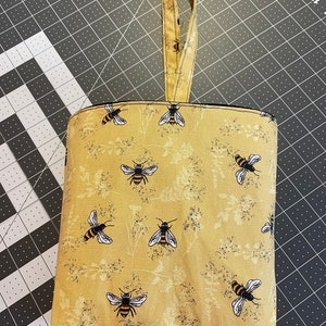 May include: A yellow fabric tote bag with a black handle and a bee pattern. The bag has a black lining and is made of a sturdy fabric.