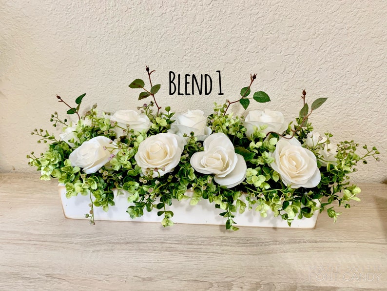May include: A white wooden box planter filled with white roses and green foliage. The text "BLEND 1" is written on the planter.