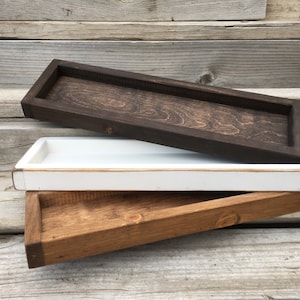 May include: Three wooden trays stacked on top of each other. The top tray is dark brown, the middle tray is white, and the bottom tray is a light brown colour.