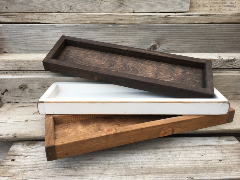 May include: Three wooden trays stacked on top of each other. The top tray is dark brown, the middle tray is white, and the bottom tray is a light brown colour.