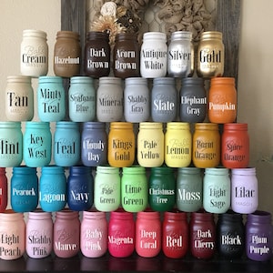 May include: A collection of 40 mason jars, each painted in a different colour and labelled with a word or phrase. The jars are arranged in four rows, with the top row being the most recent and the bottom row being the oldest. The jars are all the same size and shape, and they are all made of glass. The jars are all painted in different colours, and the words on the jars are all in black.