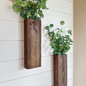 Two handmade rustic wooden wall sconces with a dark, rich wood finish. Wood color is customizable. Each planter holds a vibrant faux eucalyptus plant. Minimalist yet elegant design making this piece perfect for a rustic, farmhouse or bohemian style